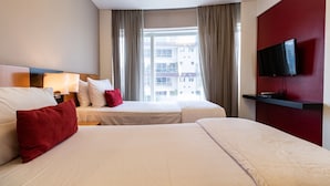 A hotel room with two beds, a TV mounted on the wall, and a window with curtains.