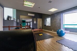 A gym with exercise equipment, a wooden floor, and a large window providing natural light.