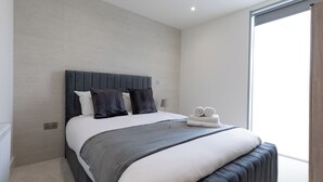 Une chambre à coucher moderne avec un grand lit, une tête de lit et une vue sur l’extérieur par une fenêtre.