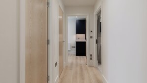 Un couloir doté d’un plancher en bois, de murs blancs et d’un espace cuisine visible au fond.