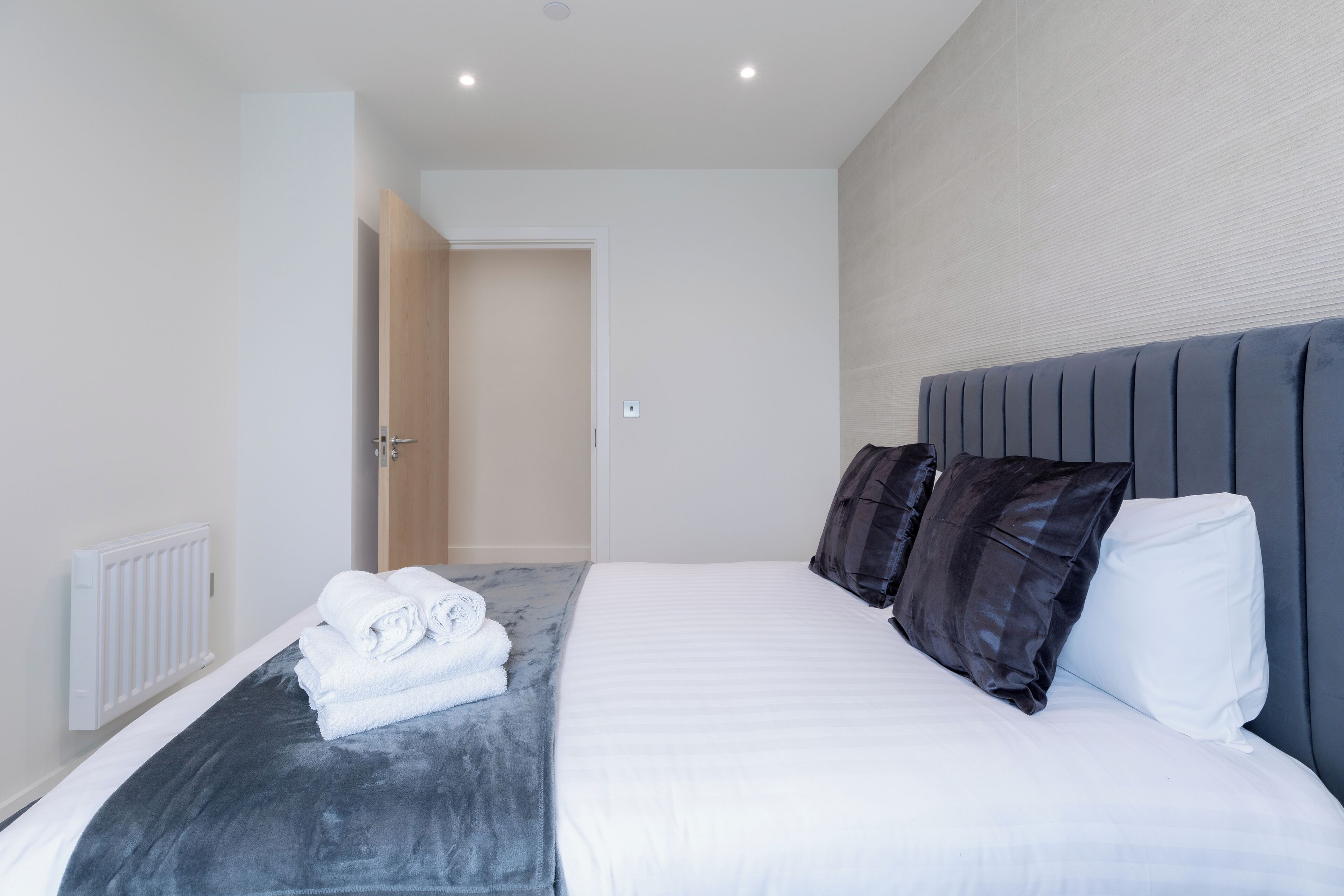 A modern hotel room with a neatly made bed, a radiator, and a door leading to another room.