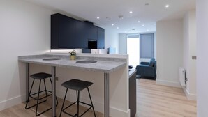 Une cuisine moderne dotée d’un îlot central, de deux tabourets de bar et d’un meuble de rangement de couleur sombre placé au-dessus.
