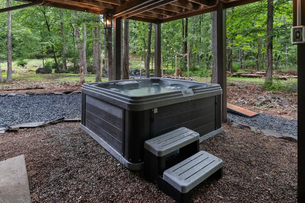 A hot tub in a covered outdoor area with steps leading up to it, surrounded by a forested landscape.