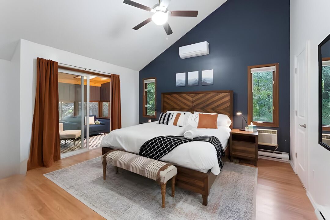 A bedroom with a bed, a bench, a nightstand, a ceiling fan, and a view of the outdoors.