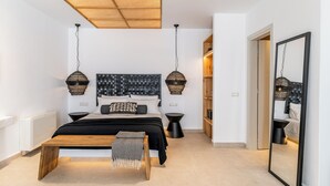 Un dormitorio moderno con una cama grande, mesitas de noche, un banco de madera y un espejo amplio.