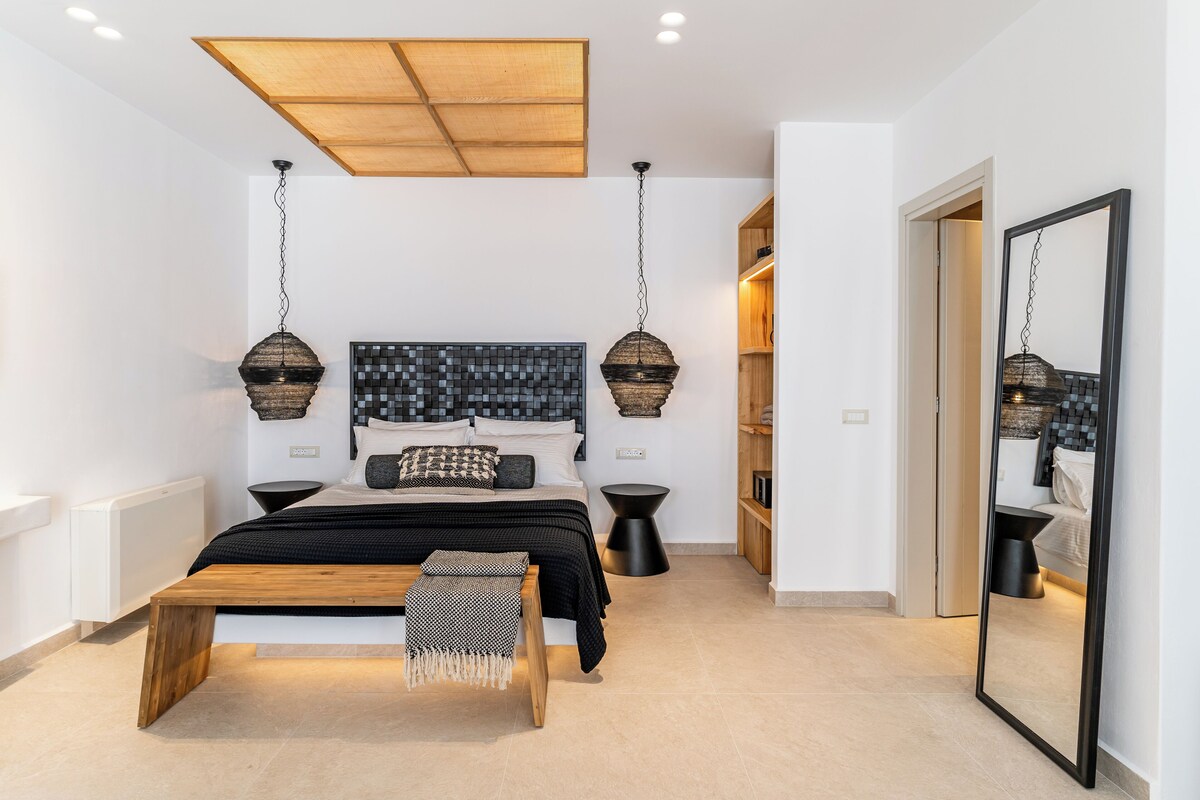 A modern bedroom with a large bed, bedside tables, a wooden bench, and a large mirror.