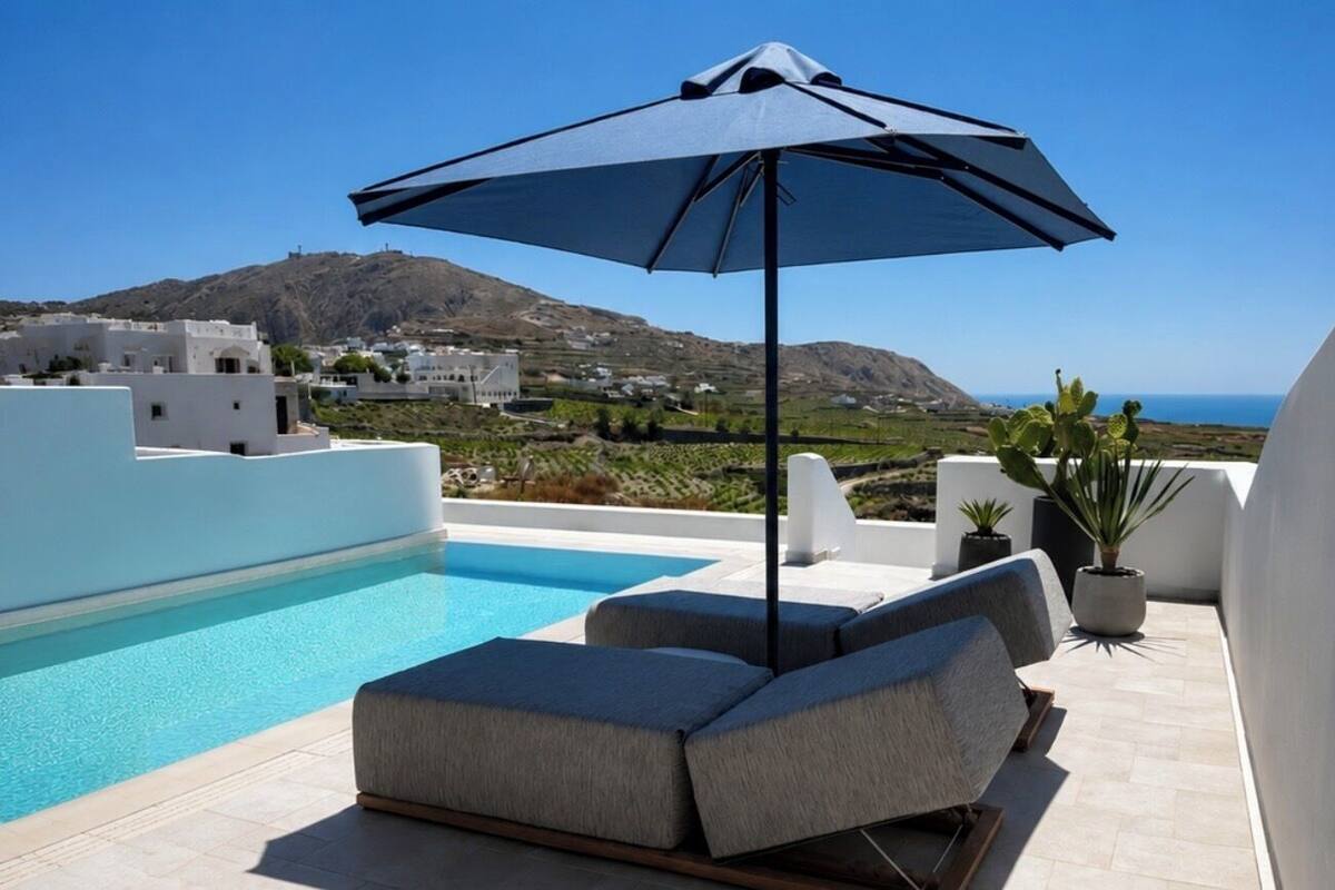 Zona junto a la piscina con una tumbona y sombrilla, con vistas a un paisaje montañoso y al mar.