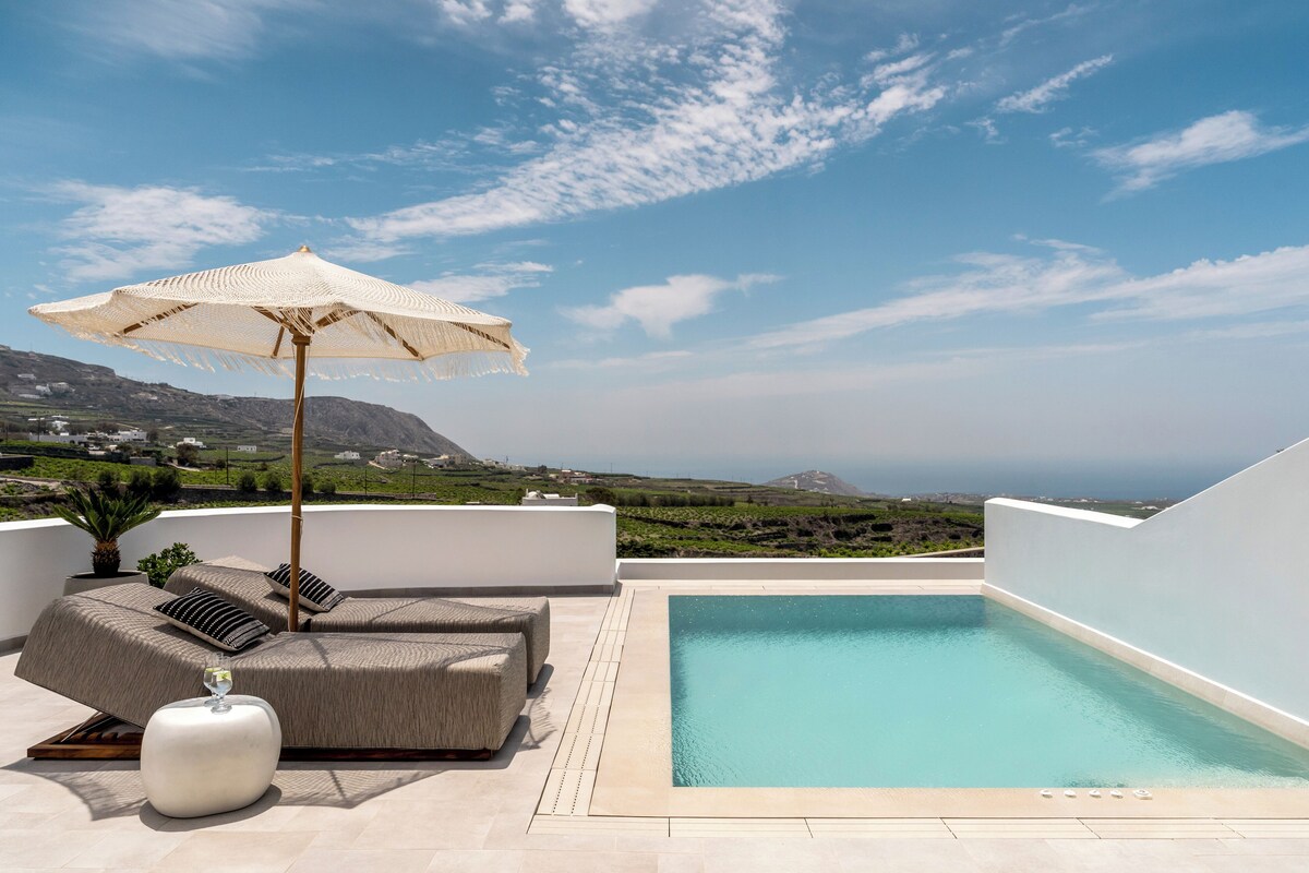 A rooftop pool area with a view of the landscape, a lounge with a sofa and pillows, and a large umbrella.