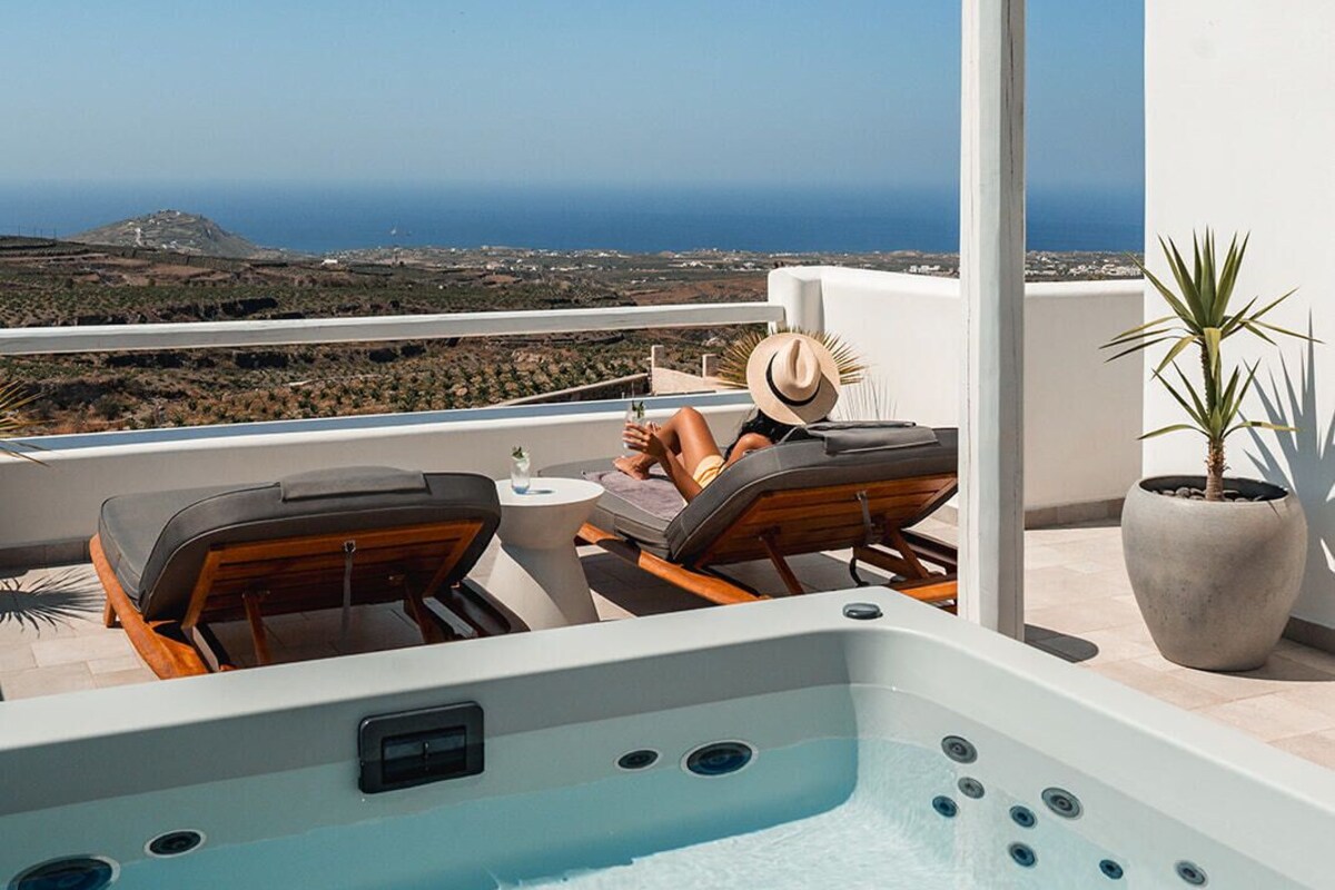 A rooftop terrace with a hot tub, lounge chairs, and a view of the ocean.