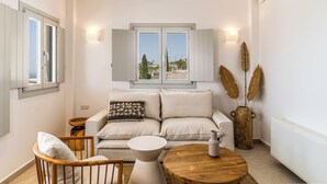 Una sala de estar moderna con sofá, una silla de madera, una mesa de centro redonda y jarrones decorativos.