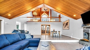 A spacious living area with a high ceiling, wooden beams, a large sofa, a coffee table, and a fireplace.