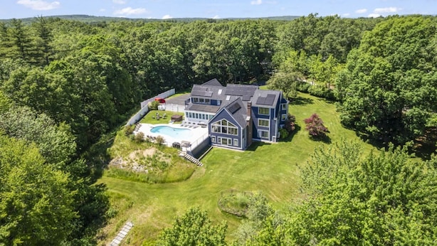 A large house with a swimming pool, surrounded by dense forest.