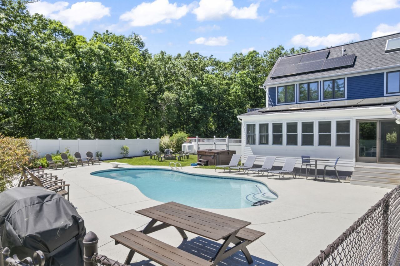 Un patio trasero con piscina, mobiliario de jardín, una parrilla y una casa con paneles solares.
