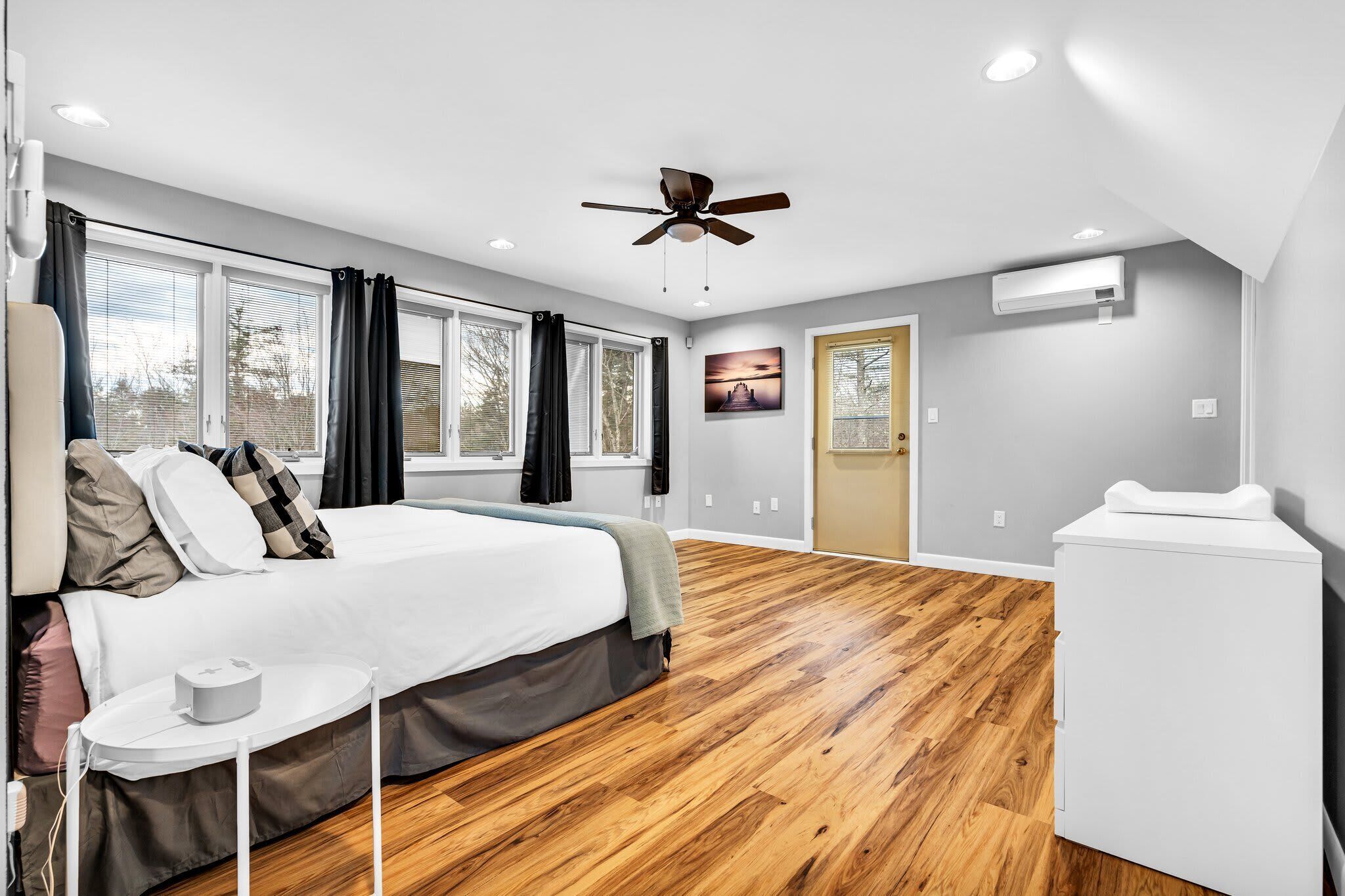 Ein modernes Schlafzimmer mit einem großen Bett, einem Deckenventilator und Blick ins Freie durch große Fenster.