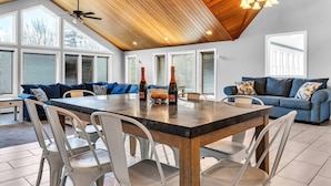 A spacious dining area with a high ceiling and large windows, a blue sofa, and a wooden dining table.