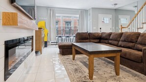A modern living room with a brown leather sofa, a wooden coffee table, and a flat-screen TV mounted on the wall. - Heart of Southie - Hot Tub + Walk to Top Bars (Boston)