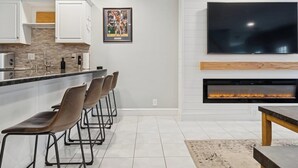 A modern kitchen with a bar area, a flat-screen TV, and a fireplace. - Heart of Southie - Hot Tub + Walk to Top Bars (Boston)