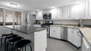 A modern kitchen with white cabinets, stainless steel appliances, a granite countertop, and a bar stool area. - Heart of Southie - Hot Tub + Walk to Top Bars (Boston)