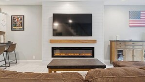 A modern living room with a flat-screen TV, a fireplace, leather sofas, and a dining area with chairs. - Heart of Southie - Hot Tub + Walk to Top Bars (Boston)