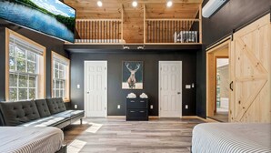 A spacious room with a loft area, a large window, a sofa, a bed, and a wooden floor.