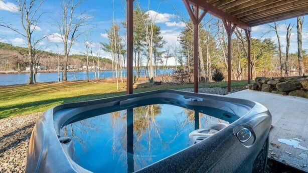 A hot tub under a wooden pergola with a view of a lake and trees.