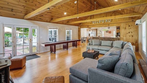 A spacious living area with a wooden ceiling, a pool table, a gray sectional sofa, and a dining area with a kitchen in the background.