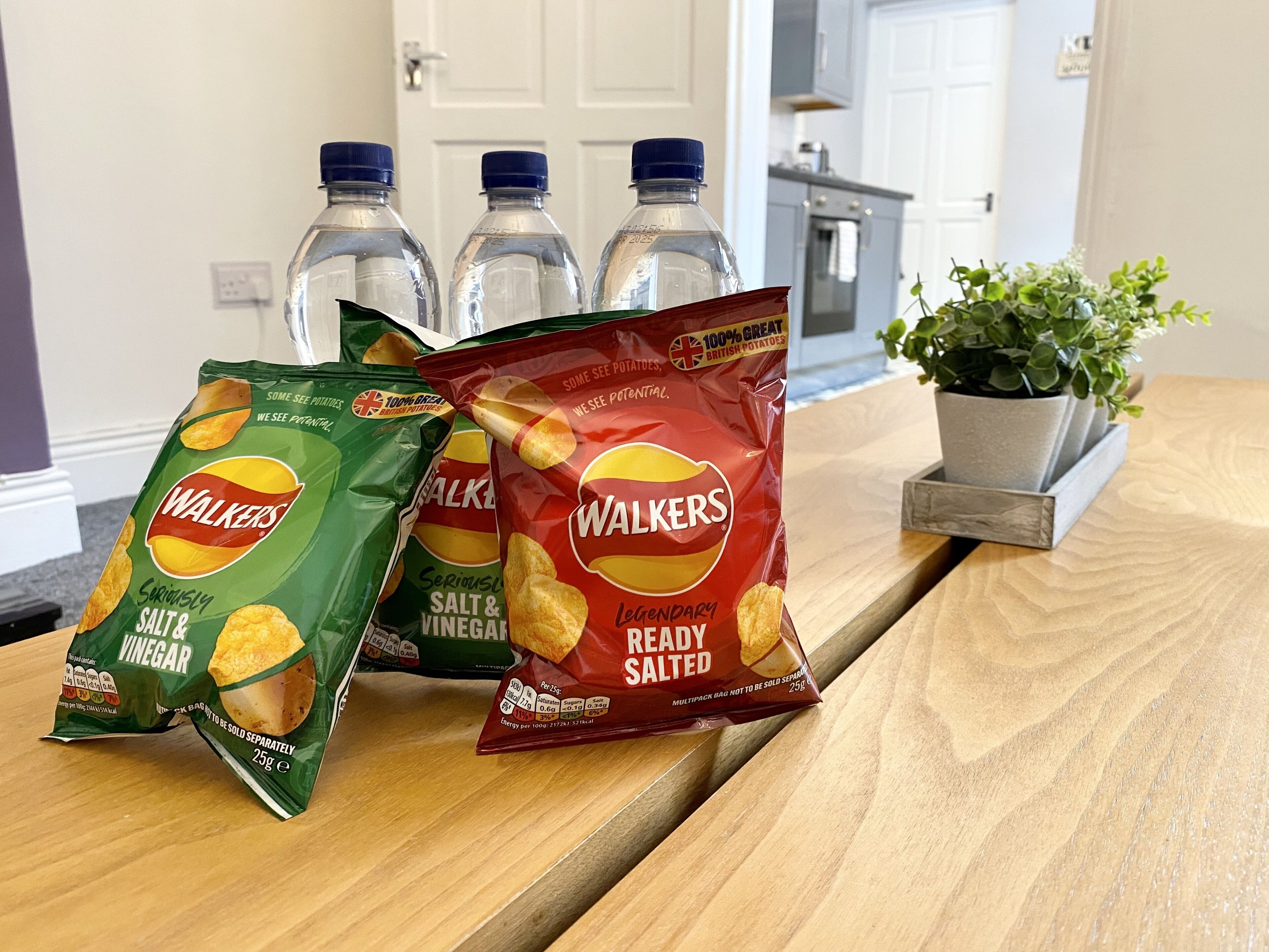 Drie zakken Walkers chips op een houten tafel, met een potplant ernaast.