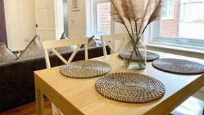 Un comedor con una mesa de madera, individuales tejidos, un jarrón con plumas de pampa y un sofá con cojines.