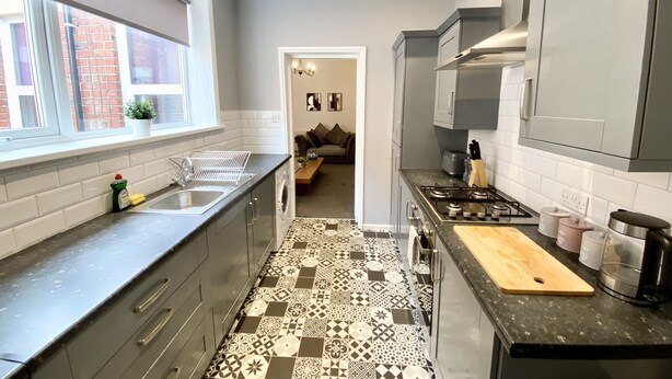 Una cocina moderna con armarios grises, piso estampado y ventana con vista a un muro de ladrillo.