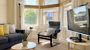 Een woonkamer met een bank, fauteuil, televisie en een kleine tafel met een plant.