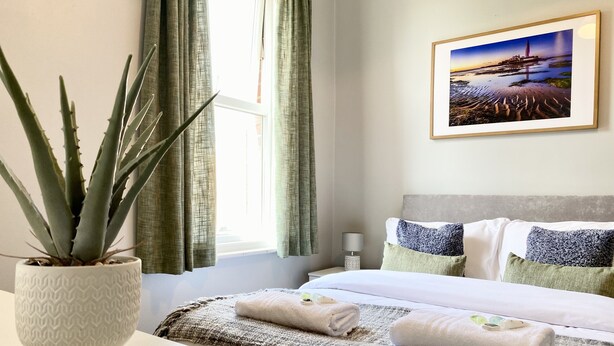 Hotelkamer met een bed, nachtkastje, lamp, ingelijst schilderij aan de muur en een kamerplant.