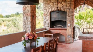 An outdoor patio with a stone fireplace, a dining table with chairs, and a flower arrangement. - Villa La Pieve - Nine Bedroom Villa, Sleeps 20 (Città della Pieve)