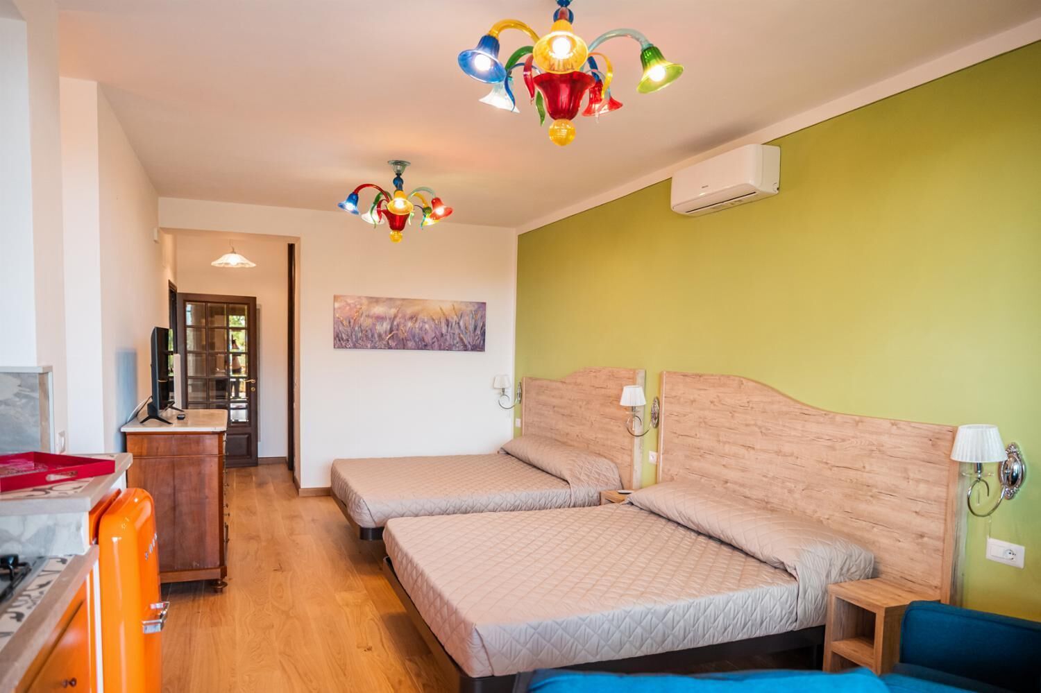 Ein Schlafzimmer mit zwei Betten, einem hölzernen Kopfteil, einem Schreibtisch, einem Stuhl und einer farbenfrohen Pendelleuchte.