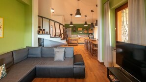 A modern living room with a sectional sofa, a flat-screen TV, and a staircase leading to a kitchen. - Villa La Pieve - Nine Bedroom Villa, Sleeps 20 (Città della Pieve)