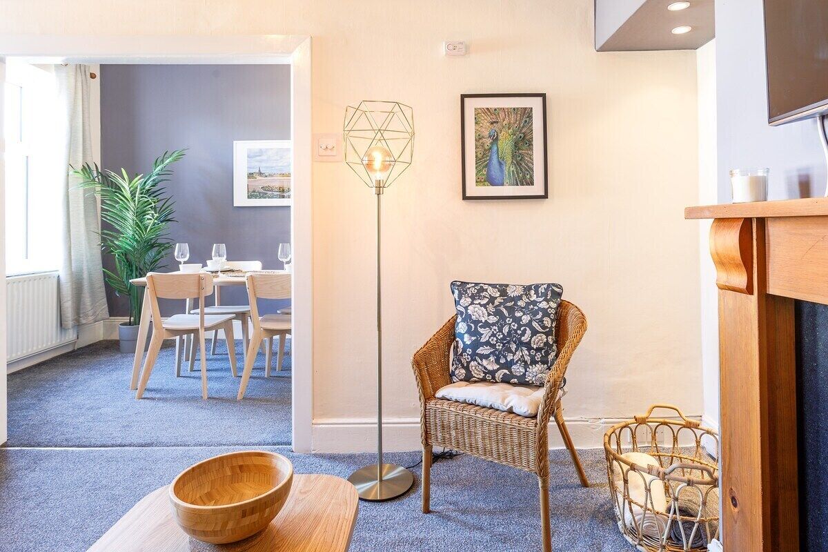 Una habitación acogedora con una silla de mimbre, una lámpara de pie y un comedor al fondo.
