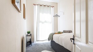 Un dormitorio con una cama, un radiador, una mesita con una planta y una alfombra blanca.