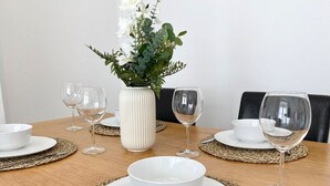 Een eettafel gedekt met witte borden, kommen en wijnglazen, met een witte vaas met bloemen en een geweven placemat.