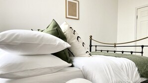 Een net opgemaakt bed met witte en groene kussens, een zwart metalen hoofdbord en een ingelijst beeld aan de muur.