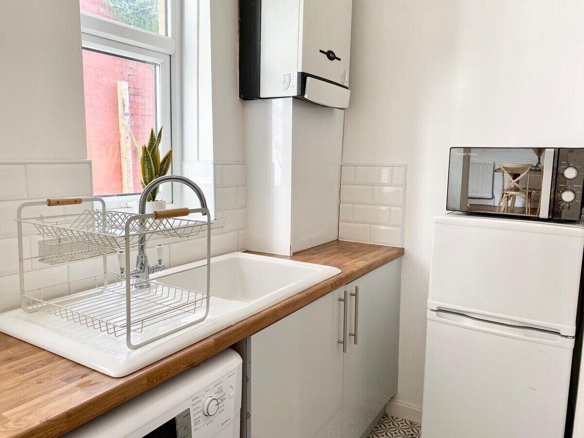 A kitchen with a white sink, wooden countertop, white cabinets, and a white refrigerator.