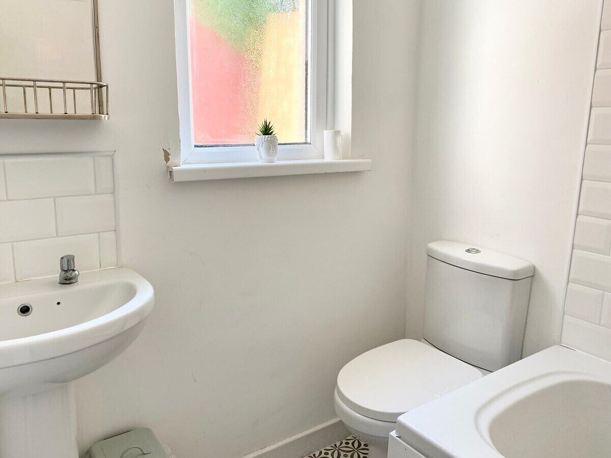Un baño pequeño y limpio con un lavamanos, inodoro y ventana blancos.
