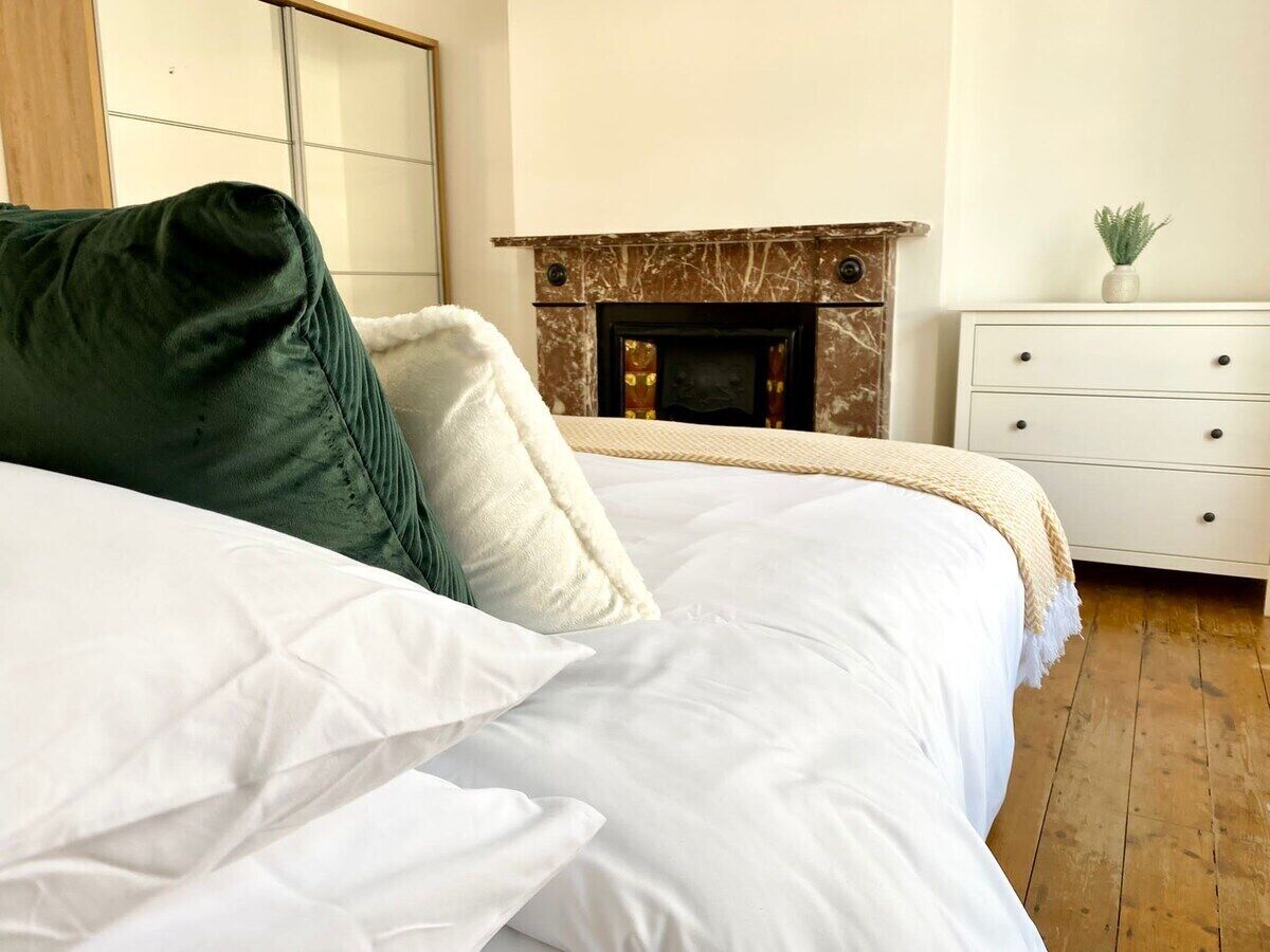 A bedroom with a bed, a fireplace, a dresser, and a mirror.