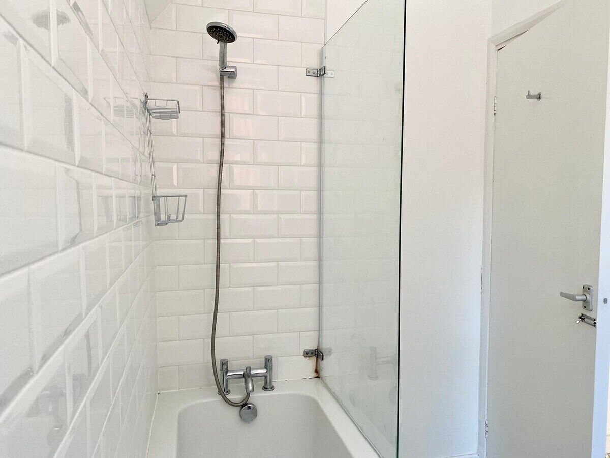 A bathroom with white tiled walls, a glass shower enclosure, a white bathtub, and a door with a handle.