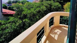 A balcony with a view of a coastal landscape, including a building with a red roof and lush greenery. - The White House on the sea (Rosignano Marittimo)