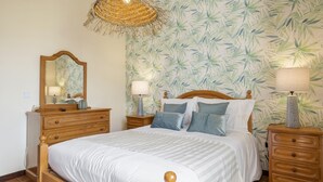A bedroom with a bed, wooden nightstands, a mirror, and a hanging light fixture. - Escapadinha do Sol by Homie (Porto Santo)