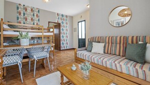 A cozy living room with a sofa, a dining table with chairs, a bunk bed, and a large mirror on the wall. - Escapadinha do Sol by Homie (Porto Santo)