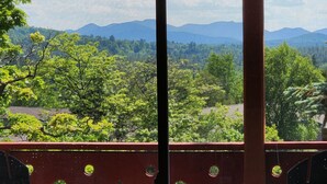 Une vue à travers une fenêtre à cadre rouge, qui révèle un paysage avec des arbres et des montagnes lointaines.