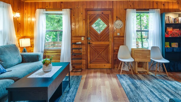 L’intérieur d’un chalet accueillant, avec une porte en bois, un canapé, une table basse, un bureau avec des chaises et une bibliothèque.