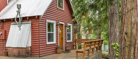 A rustic log cabin with a wooden deck, a front door, and a bench.
