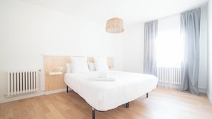 Et moderne soveværelse med sengegavl i træ, en hvid seng, et natbord og en hængende lampe.