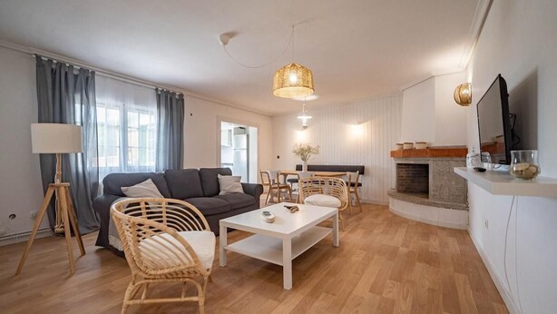 En moderne stue med sofa, sofabord, fletstole, spisebord og pejs.